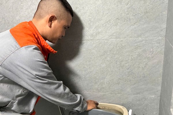 Thợ kiểm tra két nước bồn cầu khi bồn cầu chảy nước