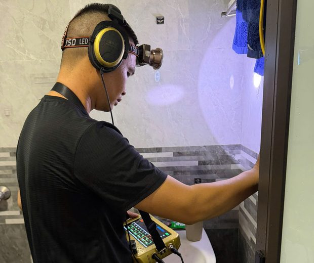 Thợ ĐNBK đeo tai nghe dùng máy siêu âm dò rò rỉ nước trong nhà vệ sinh